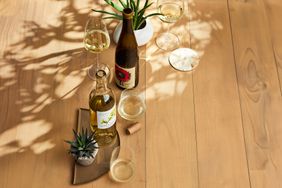 Two bottles of wine, various succulent plants and glasses of white wine on a light wooden surface. 