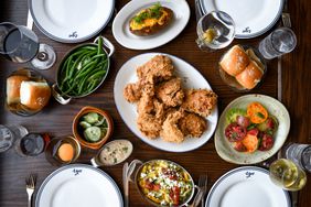 Top down view of various dishes including fried chicken, baked potatoes, green beans and colorful tomatoes at Rye in Kansas City.