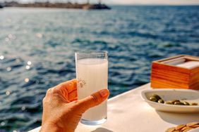 A person enjoying a glass of arak by the water. 