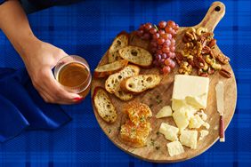 The Tillamook Maker's Reserve White Cheddar Cheese on a board with bread, grapes, nuts and honeycomb.