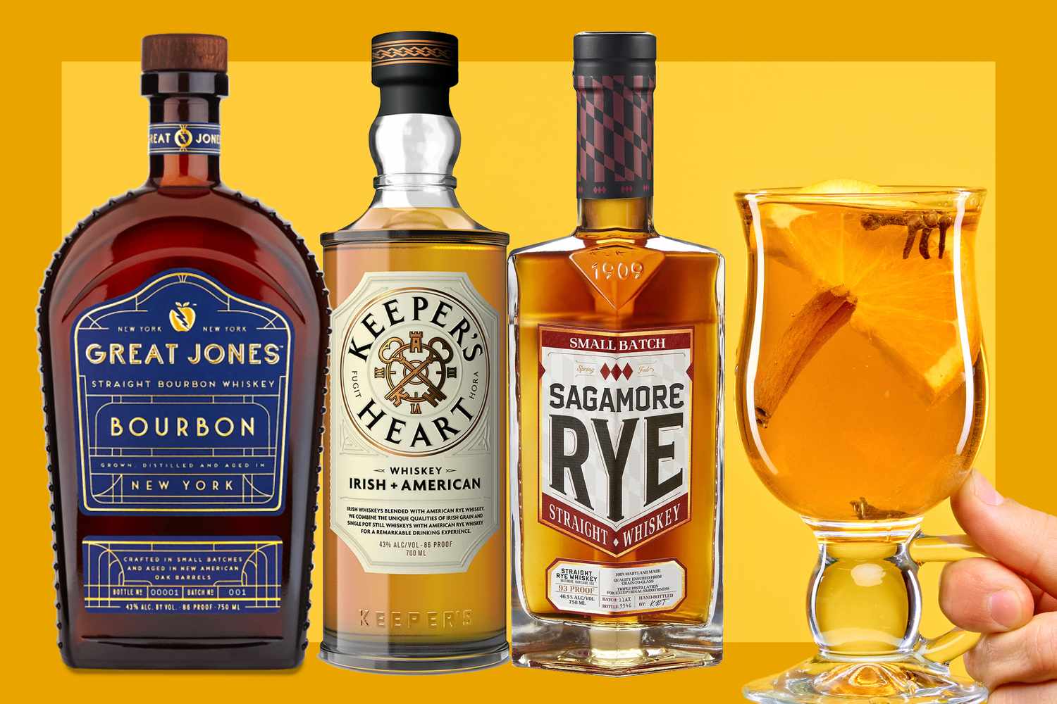 Bottles of Great Jones Bourbon, Keeper’s Heart Irish + American Blend, Sagamore Spirit Small Batch Rye and a hand holding a hot toddy on a mustard colored background. 