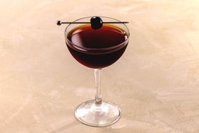 Black Manhattan cocktail in a rounded coupe glass, with maraschino cherry garnish on a metal cocktail pick