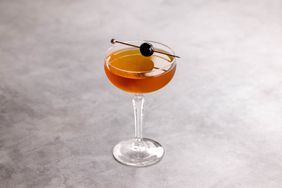 Brooklyn cocktail, light brown, in coupe cocktail glass with maraschino cherry on rim, on light grey marble background