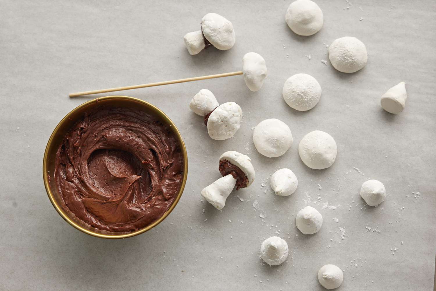 Use a wooden skewer or the tip of a small sharp knife to poke a hole into the base of each meringue mushroom cap. Dab with frosting to cement the mushroom stems to the caps.