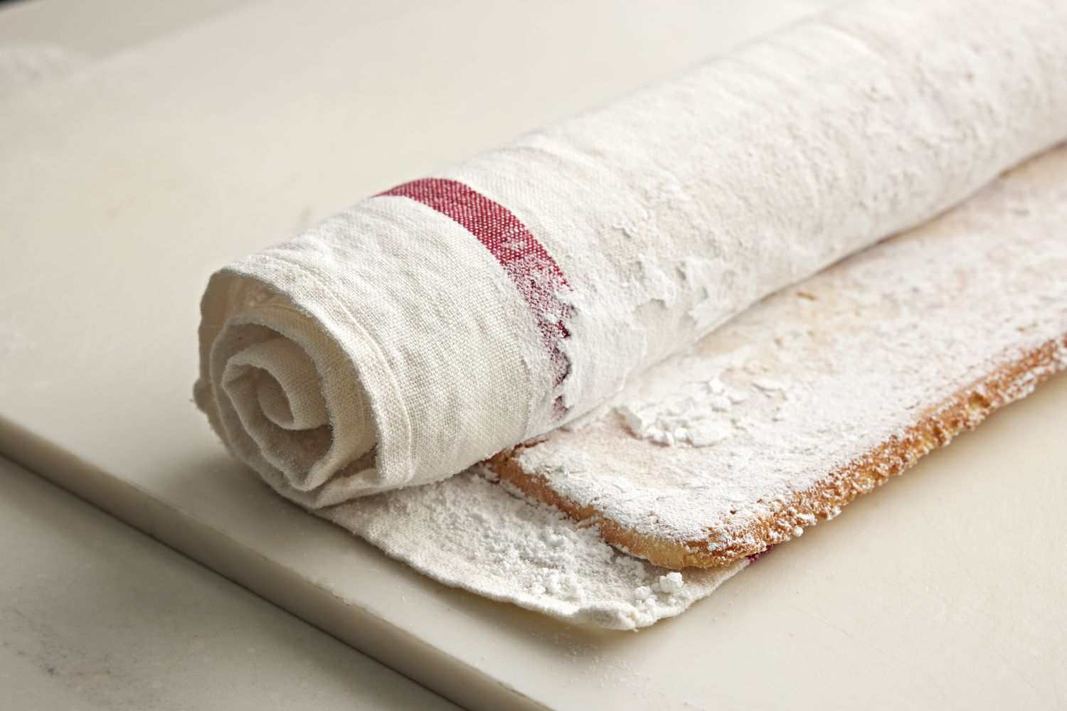 Roll up the orange sponge cake (dusted on both sides with powdered sugar) with parchment paper and a kitchen towel. Start rolling from the short side of the cake to form a log shape.