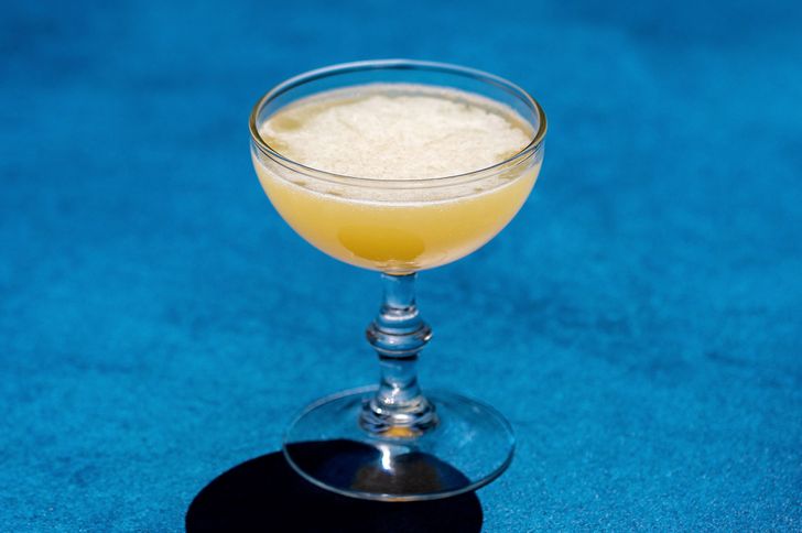 Corpse Reviver No. 2 cocktail in a curved coupe glass on a blue background