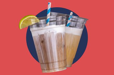 Two dirty sodas in plastic cups with striped paper straws. 