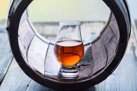 A glass of a whiskey and an old barrel.