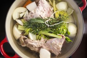 A cast iron enamel pot with parts of a turkey carcass, onion, celery, carrot and herbs for stock. 