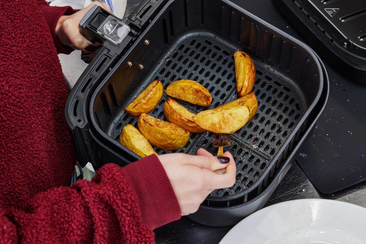 Person using a fork to flip potato wedges in the Cosori Pro Gen 2 Air Fryer