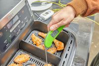 A person using a meat thermometer on chicken in the Ninja Foodi FlexBasket Air Fryer with 7qt MegaZone