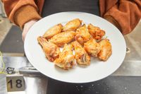 Hands holding a plate of cooked chicken wings