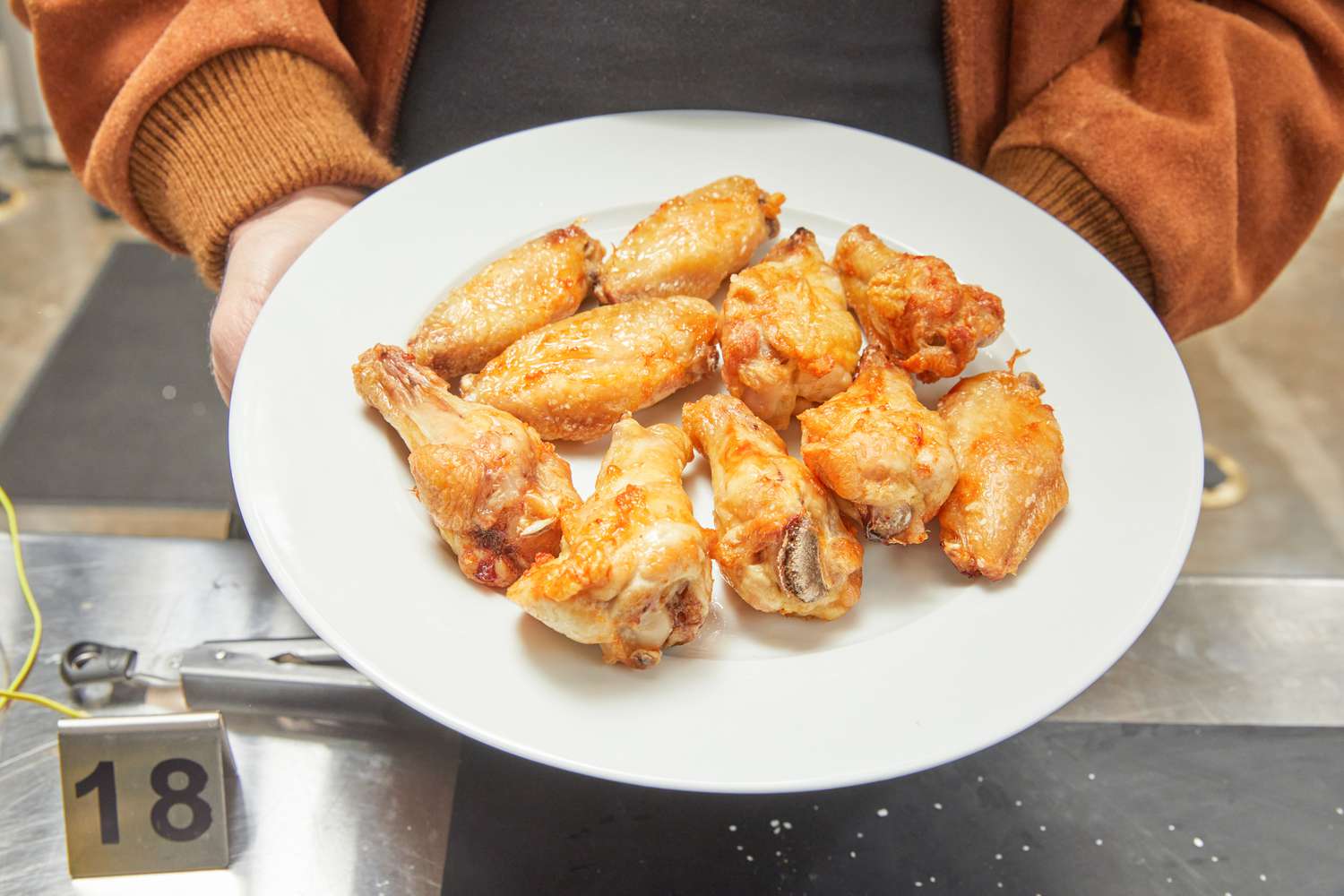 Hands holding a plate of cooked chicken wings