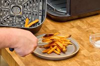 A person removes french fries from the Instant Vortex Plus 6QT XL Air Fryer