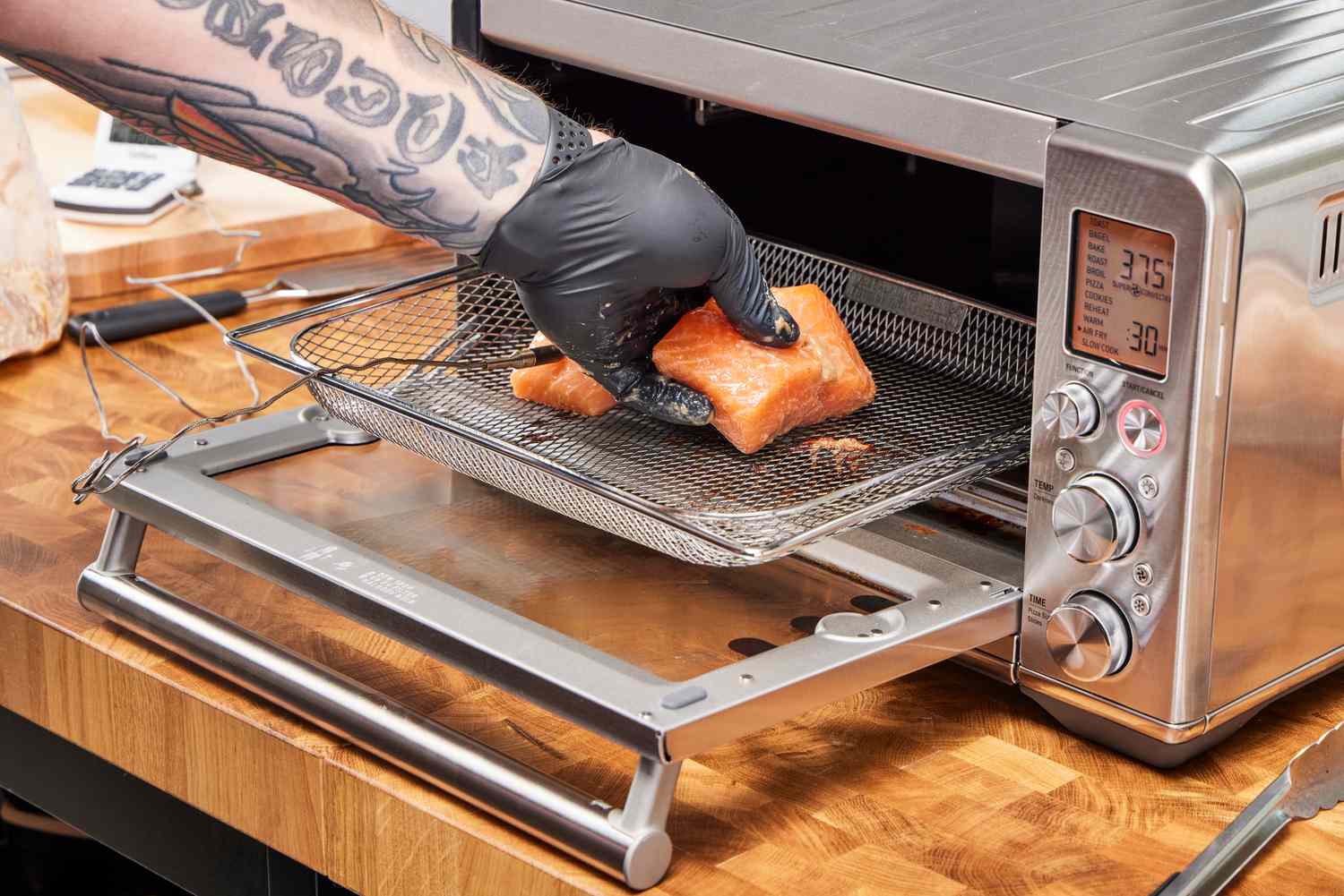 A hand placing salmon on a rack heading into the Breville the Smart Oven Air Fryer