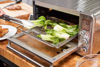 Tongs flipping vegetables on a tray in the Breville the Smart Oven Air Fryer