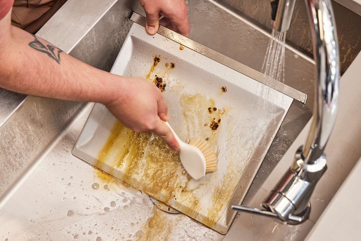 A person scrubbing a tray from inside of the Breville the Smart Oven Air Fryer in a sink