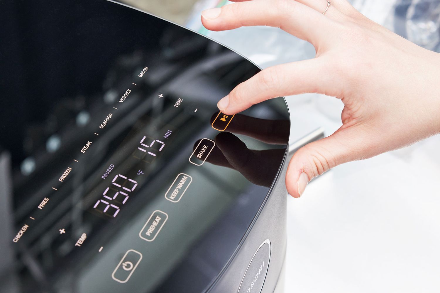 Hand pressing a button on the Cosori 9-in-1 5-Quart Air Fryer