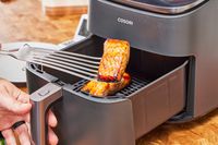 A person removing cooked salmon from the COSORI TurboBlaze 6.0-Quart Air Fryer