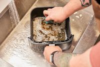 A person scrubbing the basket of the COSORI TurboBlaze 6.0-Quart Air Fryer in a sink