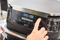 Hand pressing a button on the Ninja DZ071 Foodi FlexBasket Air Fryer with 7qt MegaZone