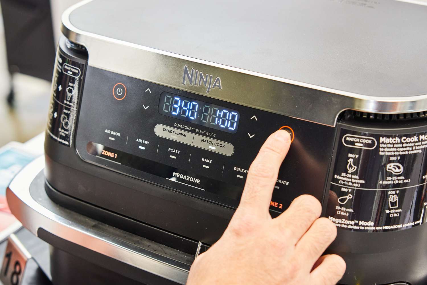 Hand pressing a button on the Ninja DZ071 Foodi FlexBasket Air Fryer with 7qt MegaZone