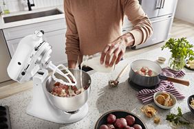 A person pouring heavy cream into a KitchenAid batter bowl filled with boiled potatoes