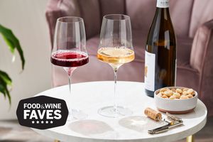 Two wine glasses containing red and white wines displayed on white table with wine bottle, corkscrew, and bowl of nuts