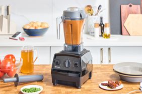 Orange liquid int he Vitamix Explorian 310 on a wooden counter next to other items