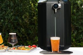 The iGulu F1 Smart Beer Brewing System on a table outdoors with full glasses of beer and plates of food