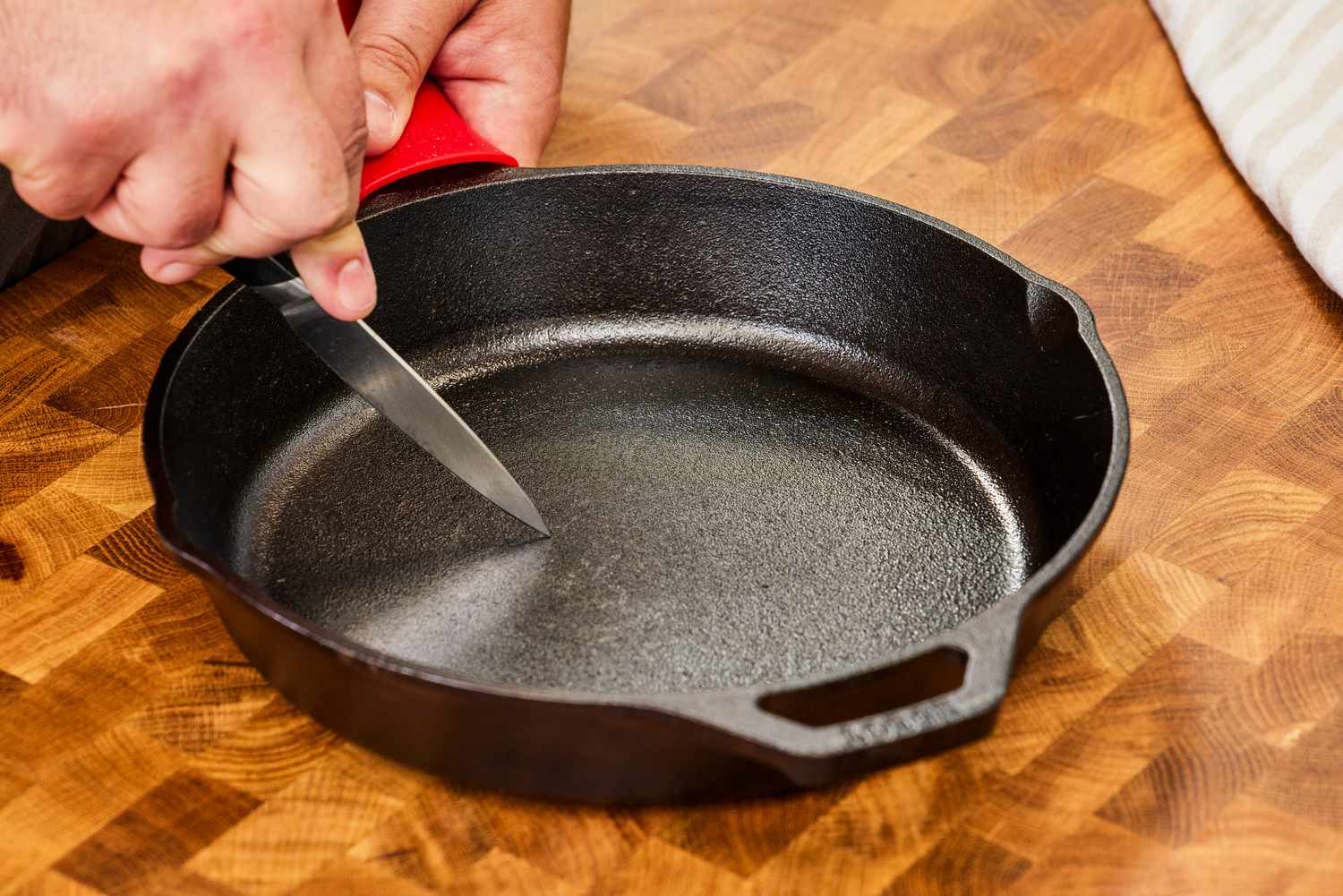 A person uses a knife on the bottom of the Lodge Cast Iron Skillet