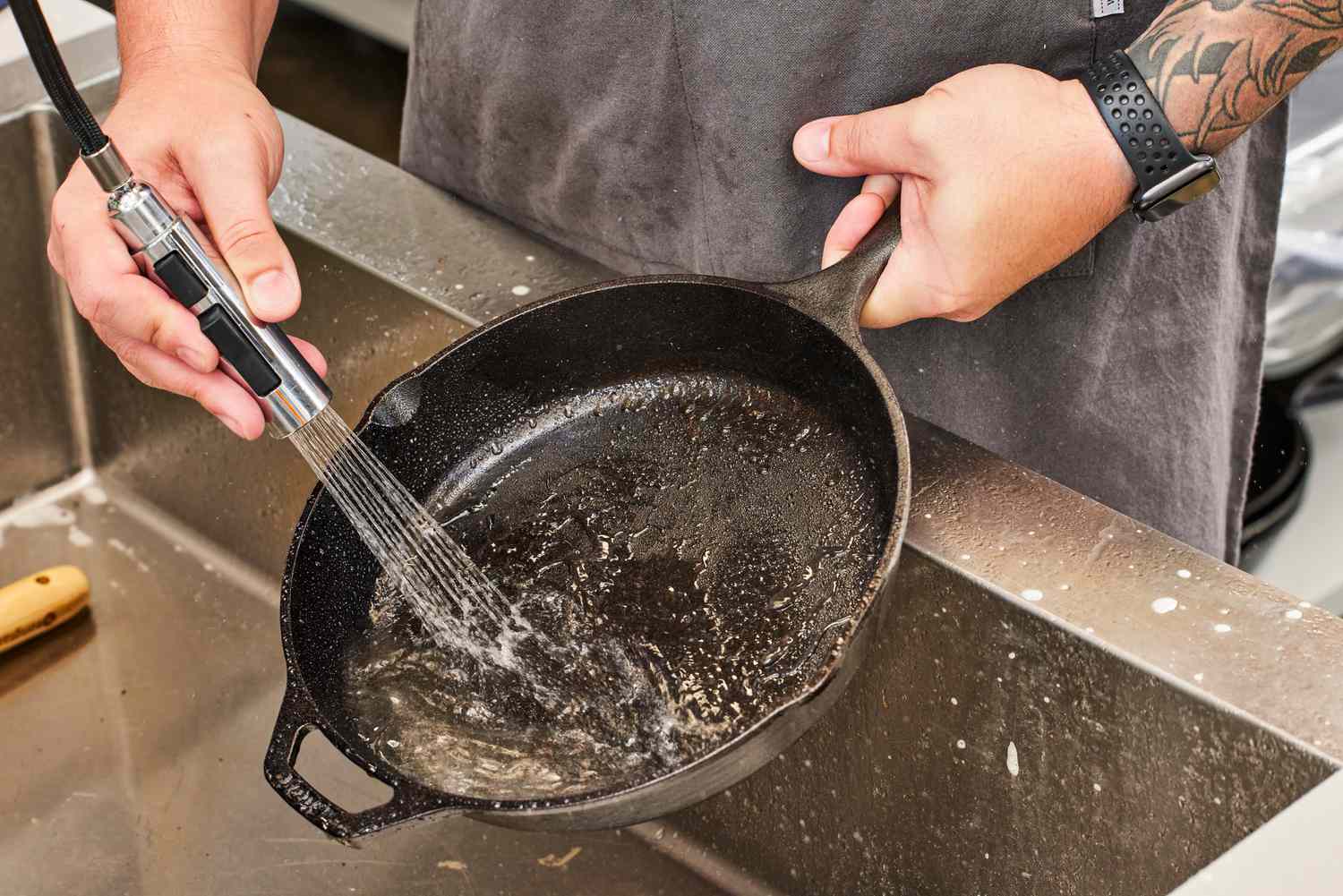 A person sprays water into the Lodge Cast Iron Skillet over a sink