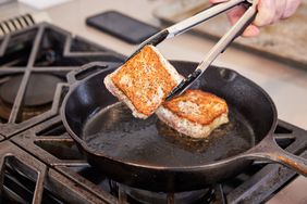 Hand using tongs to flip fish in a Lodge Cast Iron Skillet