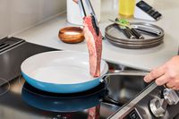 A person places raw meat onto the GreenPan Nova Ceramic Nonstick 10-Piece Cookware Set pan