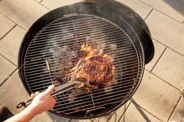 Person grilling meat using the Weber Original Kettle Premium 22-Inch Charcoal Grill