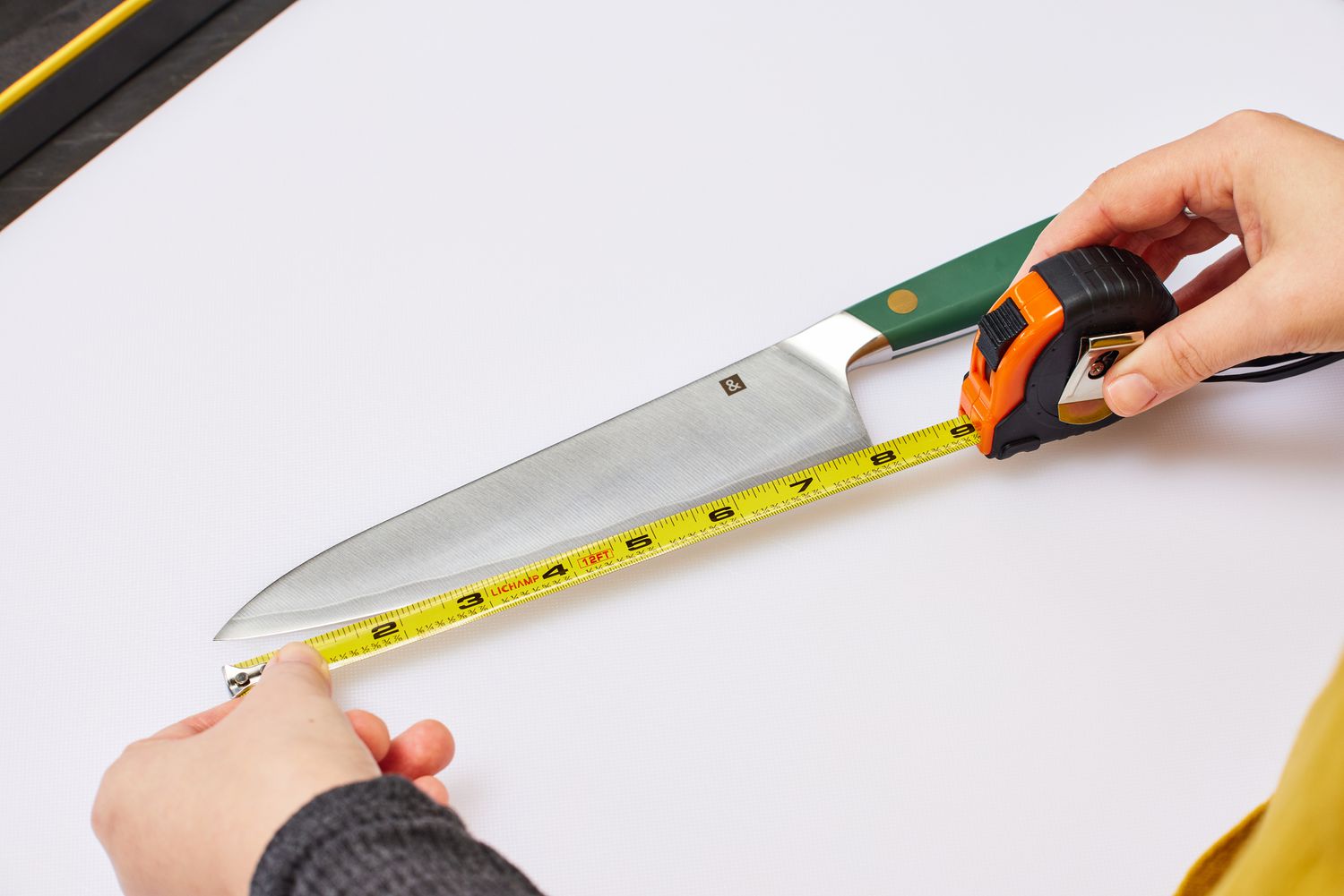 Hands use a tape measure to measure the blade of a Hedley & Bennett 8-Inch Chefâs Knife