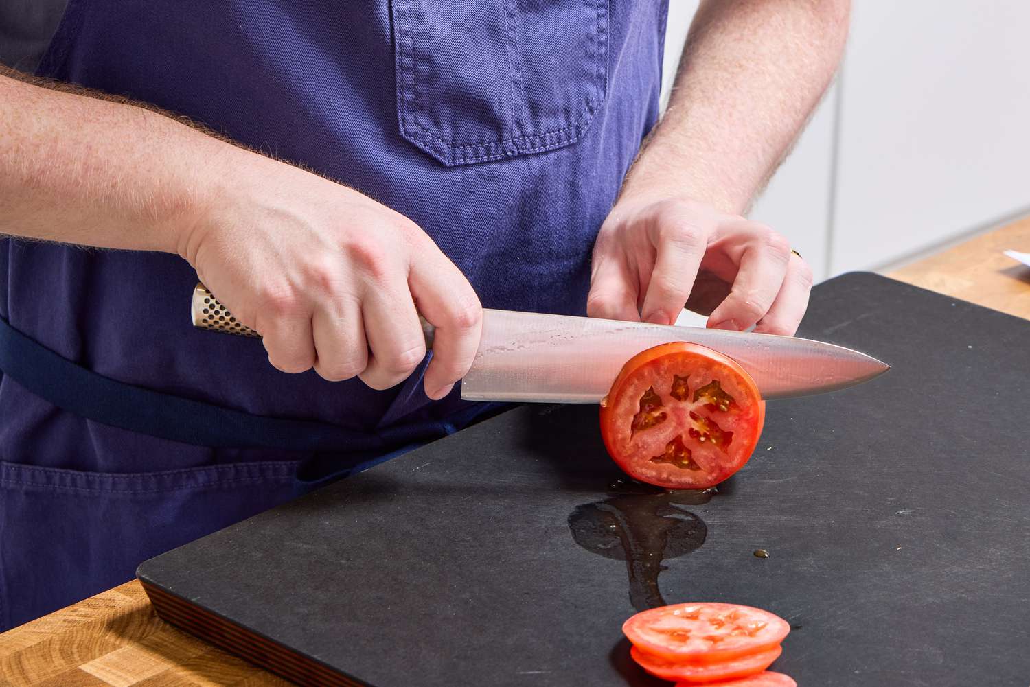 A person slices a tomato with the Global Classic 8-Inch Chef's Knife