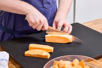 A person slices sweet potato with the Global Classic 8-Inch Chef's Knife on a cutting board