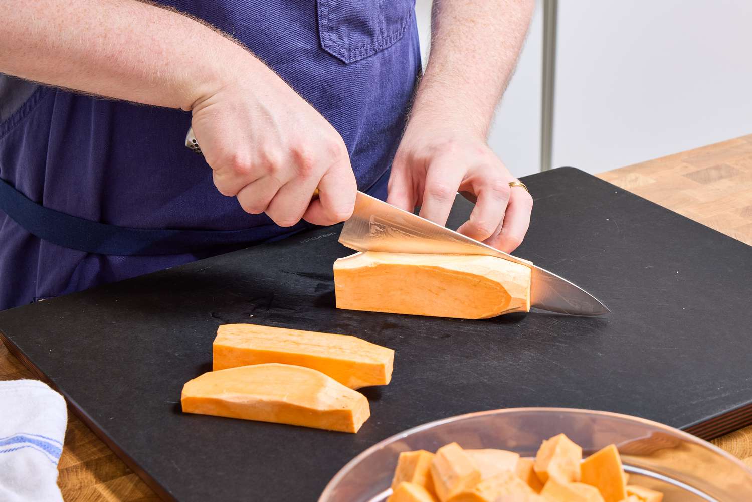 A person slices sweet potato with the Global Classic 8-Inch Chef's Knife on a cutting board