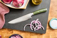 The HexClad 8 Inch Damascus Steel Chef’s Knife on a cutting board with sliced onions