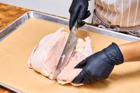 A person cuts chicken with the HexClad 8 Inch Damascus Steel Chef’s Knife