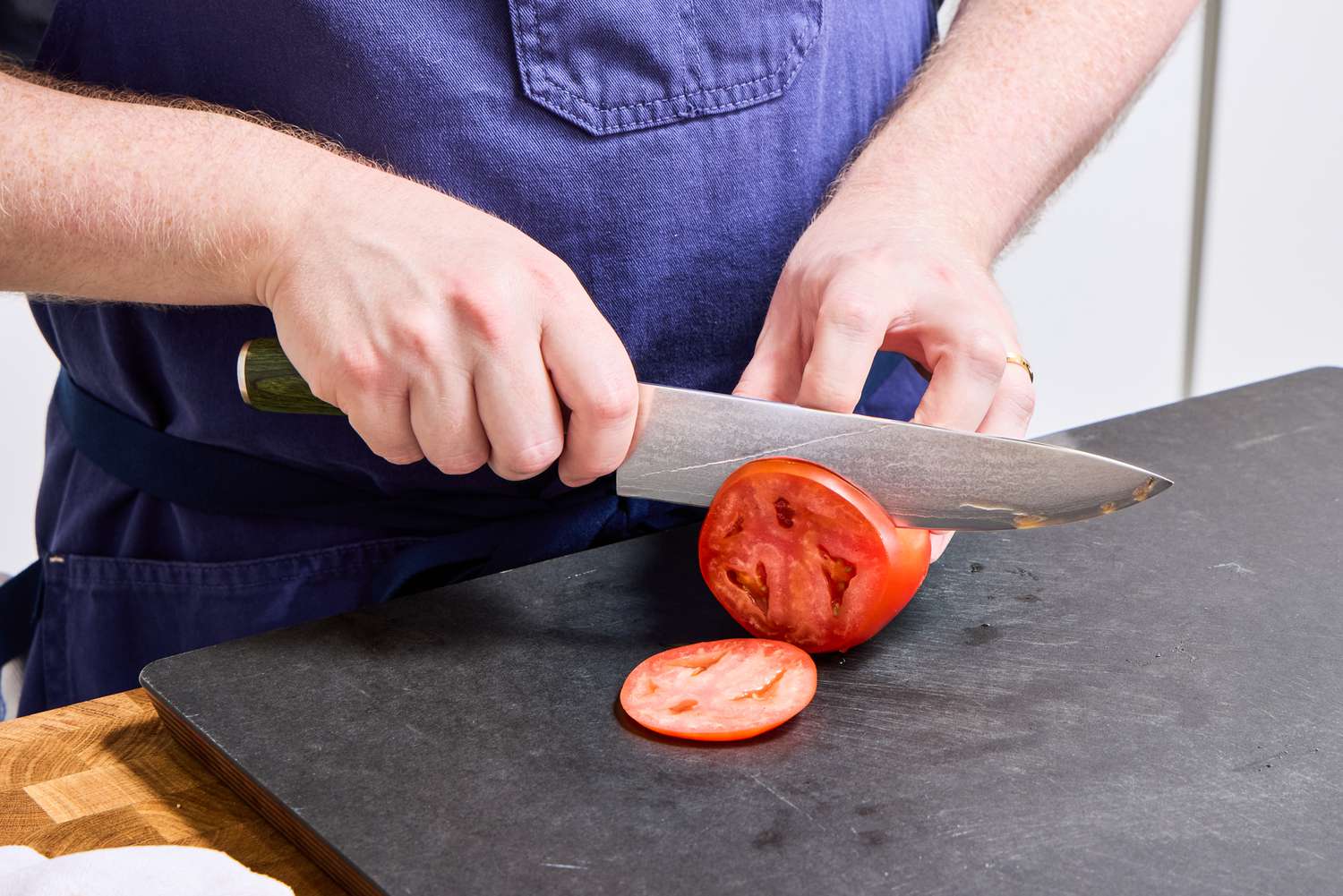 A person slices a tomato with the HexClad 8 Inch Damascus Steel Chef’s Knife