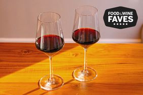 Two wine glasses sitting on a wooden surface and filled with red wine