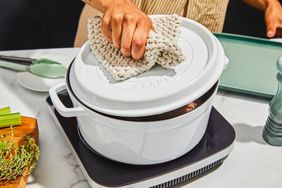 A person opening the lid of the Staub Cast Iron 5.5-Quart Round Cocotte