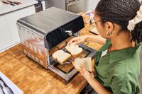 A person placing slices of bread in the Instant Omni Plus Air Fryer Toaster Oven