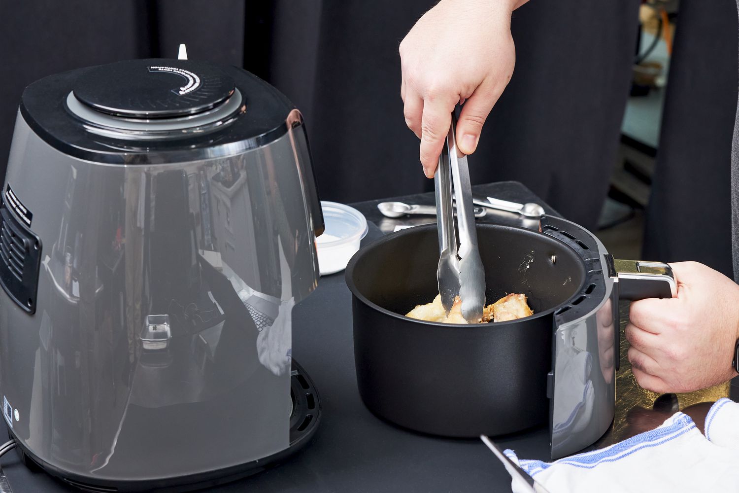 Person using tongs to pick up chicken in Ninja 4-Quart Air Fryer