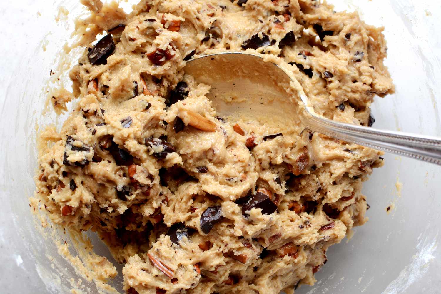 Raw cookie dough being mixed with chocolate chunks and chopped pecan nuts.