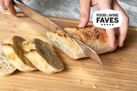 Hands using Zwilling Pro 9-inch Bread Knife Z15 Serration to cut loaf of bread on cutting board