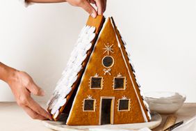 A person putting together an A-frame gingerbread house. 