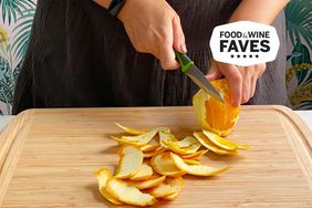 Hands cutting peel away from orange with paring knife